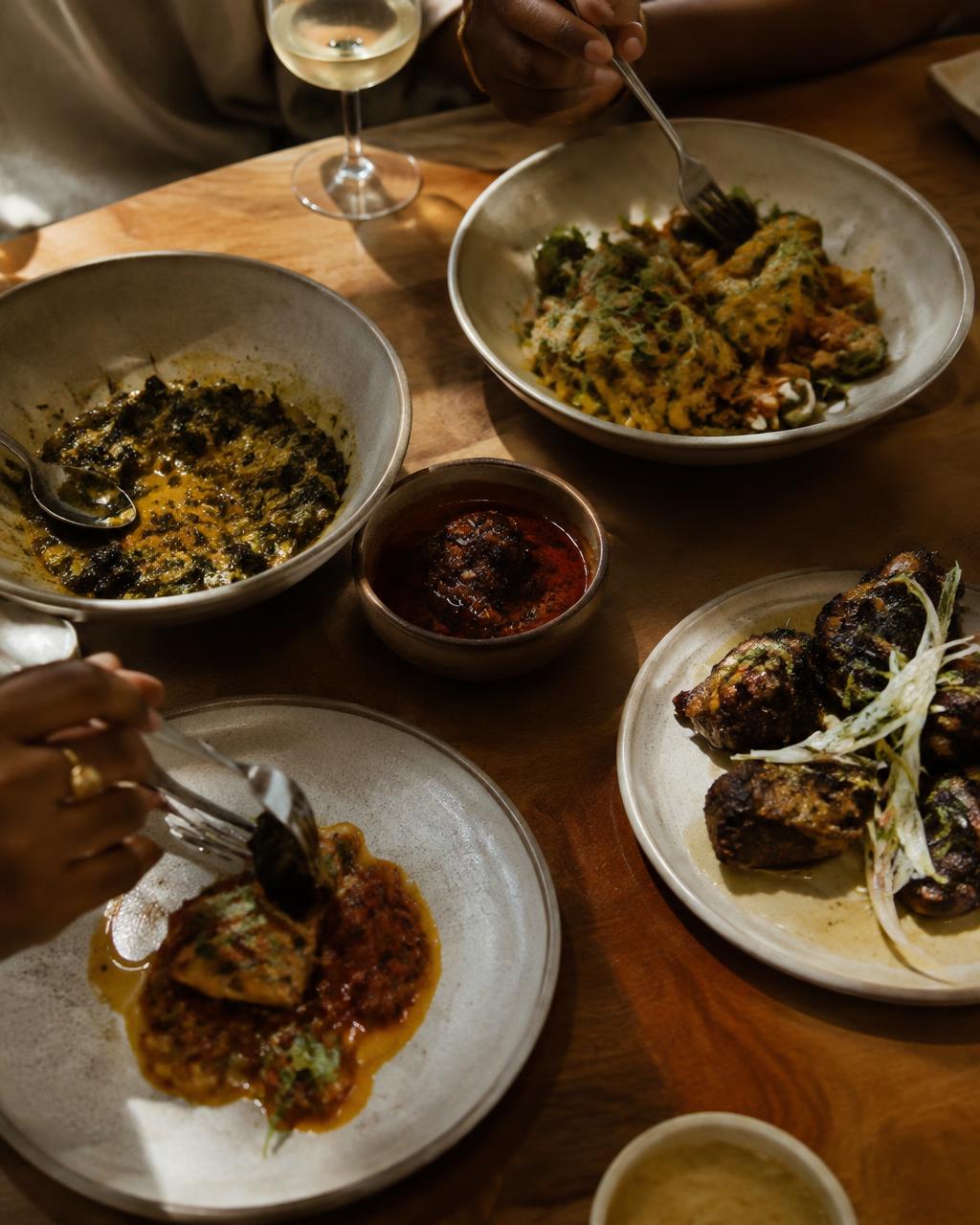Hands reaching across shared plates at a wooden table